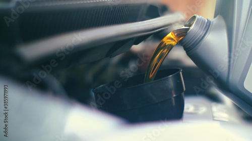 Pouring fresh new clean synthetic oil into car's engine, closeup.