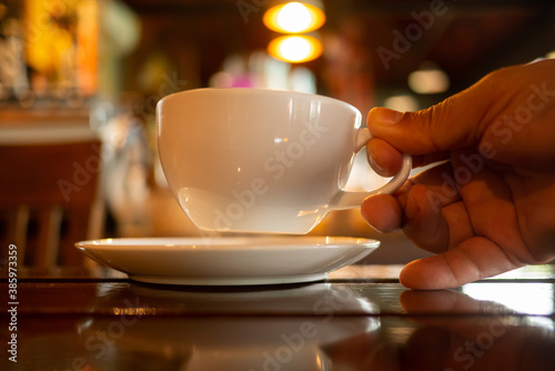 A white coffee cup in hand on blurred cafe background vintage style.