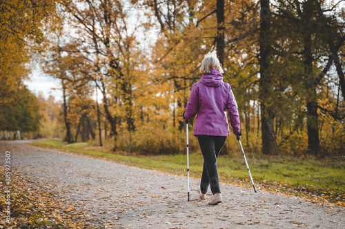 an elderly woman walks through the Park on Scandinavian sticks