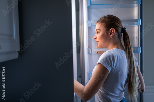Night bite. Cheerful mature woman opening refrigerator and posing in profile
