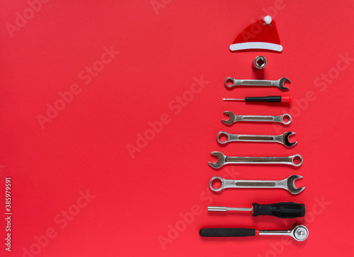 Christmas tree made of construction tools with a New Year's red hat on a red background. New Year Concept for auto workshop. Flat lay, copy space, top view