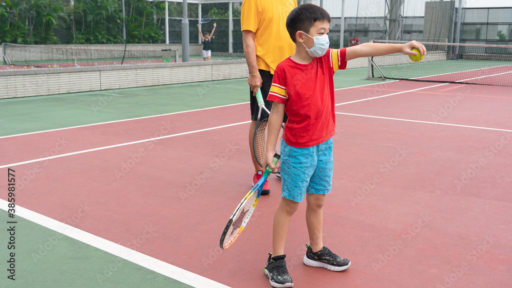 A young boy with the tennis coach.The kid is learning with the instructor.A parent teaches a son playing techniques. Kids tennis on the big court. Tennis school or club. A young boy with the tennis coach.The kid is learning with the instructor.A parent teaches a son playing techniques. Kids tennis on the big court. Tennis school or club.