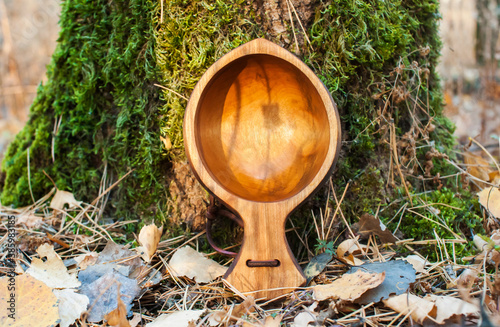 Beautiful traditional Finnish wooden mug  Kuksa  in the autumn forest on a background of wood and green moss