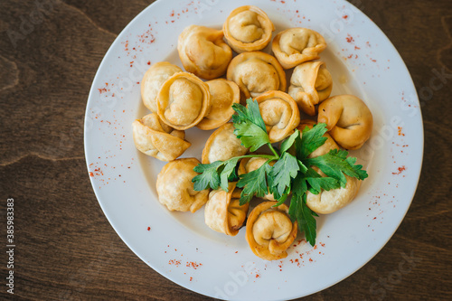 Fried dumplings with green parsley leaves on a white plate. A portion of meat in the dough. Russian dish on a wooden table