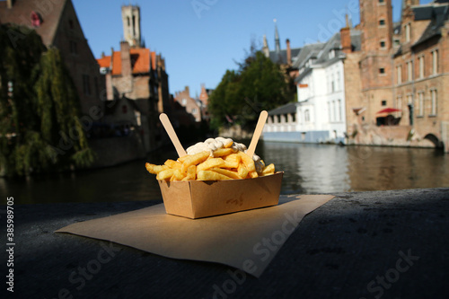 The traditional street food snack, the Belgian Fries with pepper sauce pictured on the wall over the channel in Bruges in Belgium. 