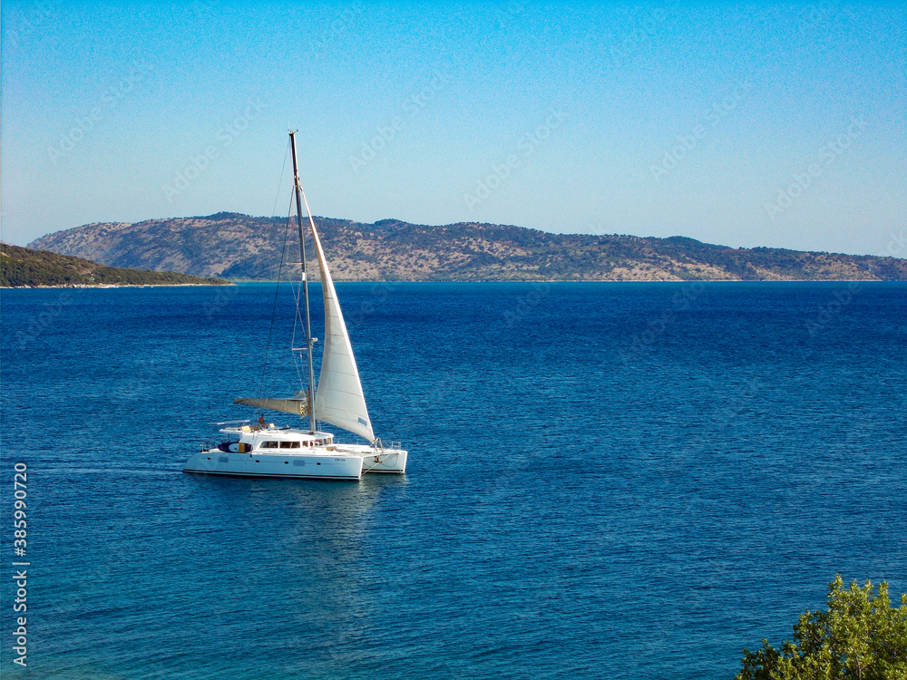 White catamaran yacht sailing boat alone on blue sea and cloudless sky