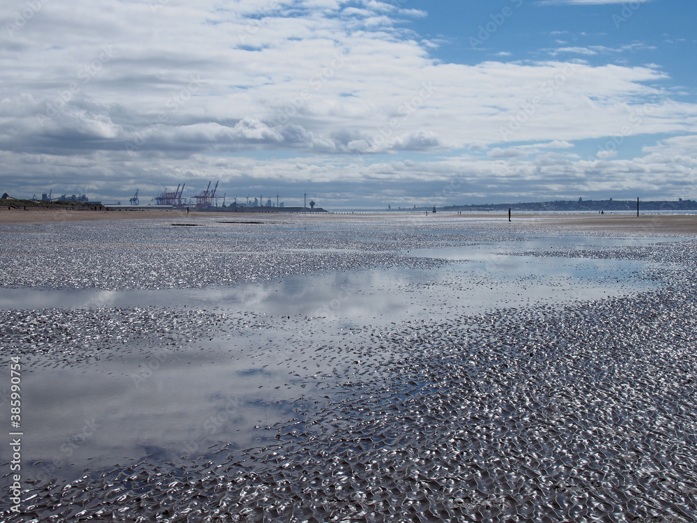 the beach at blundell sands near southport with water from the incoming tide reflecting the sky and liverpool city and container terminal and cranes visible in the distance the beach at blundell sands near southport with water from the incoming tide reflecting the sky and liverpool city and container terminal and cranes visible in the distance