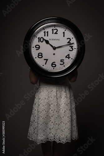 Studio portrait of girl in white dress holding large clock in dark rembrandt style photo