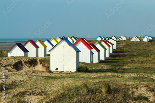 The tiny white beach cottages with colorful roofs at a beach by Gouville-sur-Mer in France in Normandy. The attraction for the tourists.  © shootingtheworld
