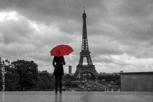 The lady with a red umbrella is standing in front of the Eiffel tower in Paris in France. Black and white picture with isolated red umbrella. 