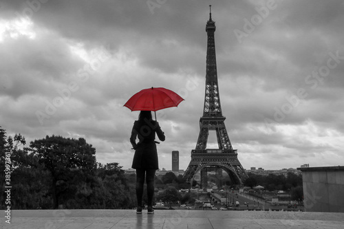 The lady with a red umbrella is standing in front of the Eiffel tower in Paris in France. Black and white picture with isolated red umbrella.  © shootingtheworld