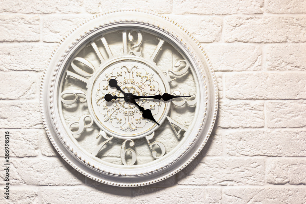 white, vintage wall clock on a white brick wall.