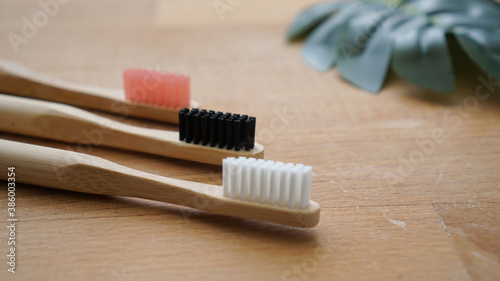 Pink  black and white color of eco-friendly bamboo toothbrushes with blurred leaf on a wood background. Natural organic dental concept
