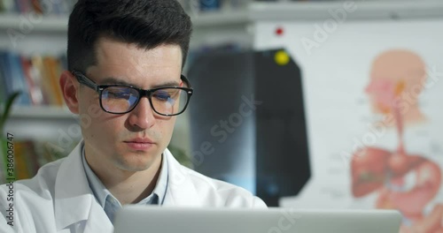 Wallpaper Mural Close up of male doctor in glasses looking at laptop screen while working. Man in white professional rob while sitting in medical office. Concept telemedicine and telehealth Torontodigital.ca