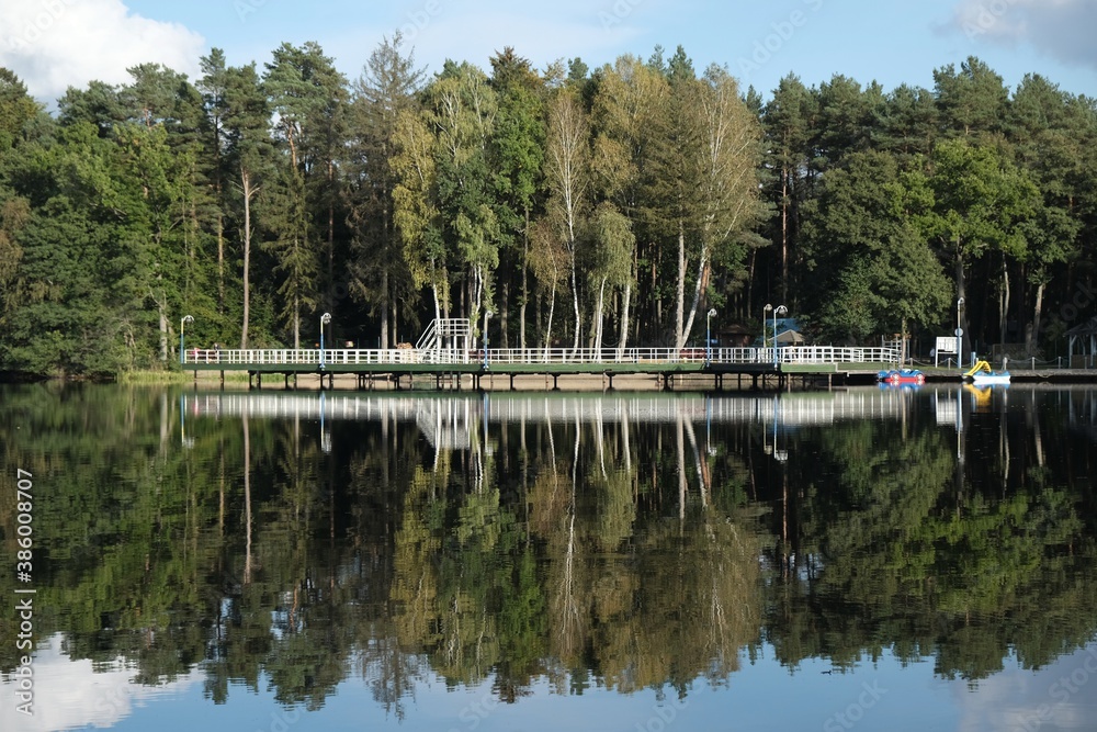 Fototapeta premium Pier and holiday resort on the lake by the forest. Beautiful reflection in the water.