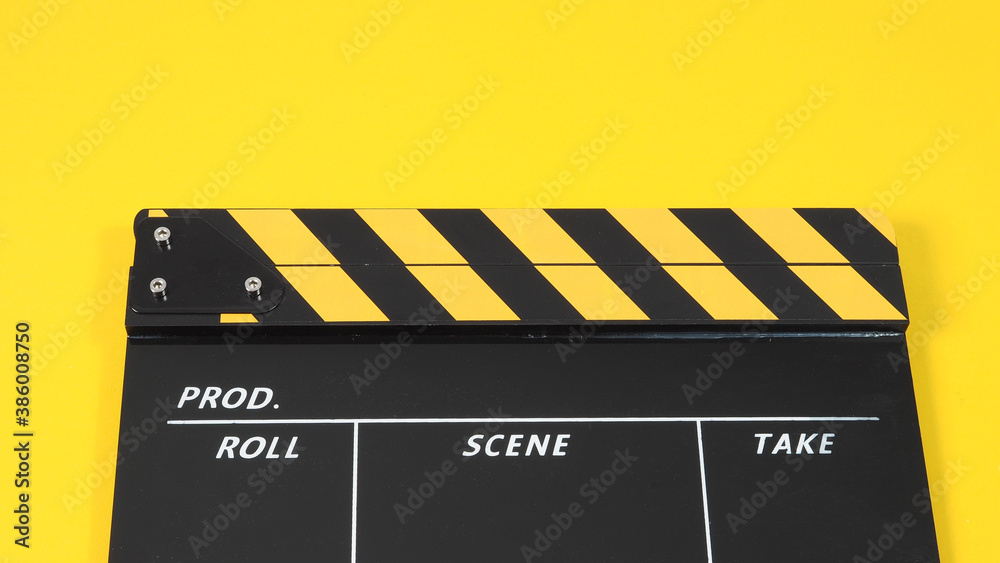 Naklejka premium Clapperboard or movie slate with black&yellow color and film roll on yellow background. It is used in video production and film industry.