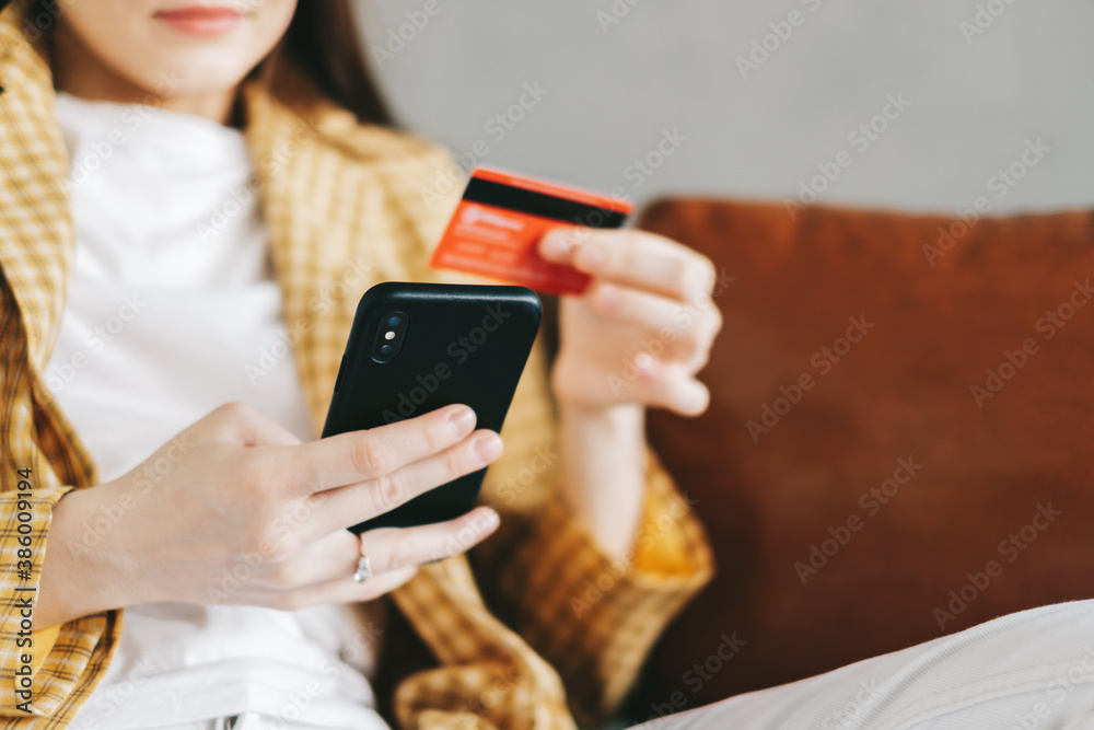 Young caucasian woman holding credit card, using smartphone and shopping online. E-commerce, internet banking, spending money.