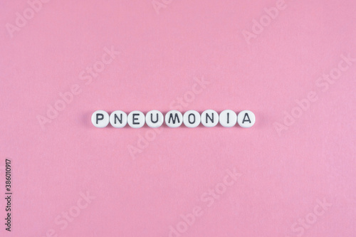 The inscription "Pneumonia" is laid out in a row of round white counters with black letters. Close-up on a pink background. Billet for design.