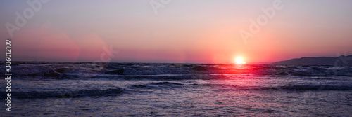 bright red bowl of sun with sunrays under sea water surface in sunrise or sunset