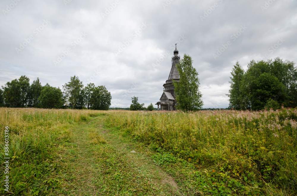 August, 2020 - Red Lag. Abandoned tall wooden church in the middle of a large field. Russia, Arkhangelsk region
