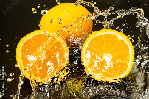 Fototapeta Naklejka Na Ścianę i Meble -  two oranges, whole and cut in half with drops and splashes of water on dark glass with gradient background and reflection