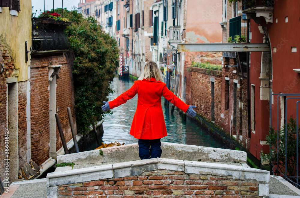 Donna con un cappotto arancione sul ponte del diavolo a Venezia
