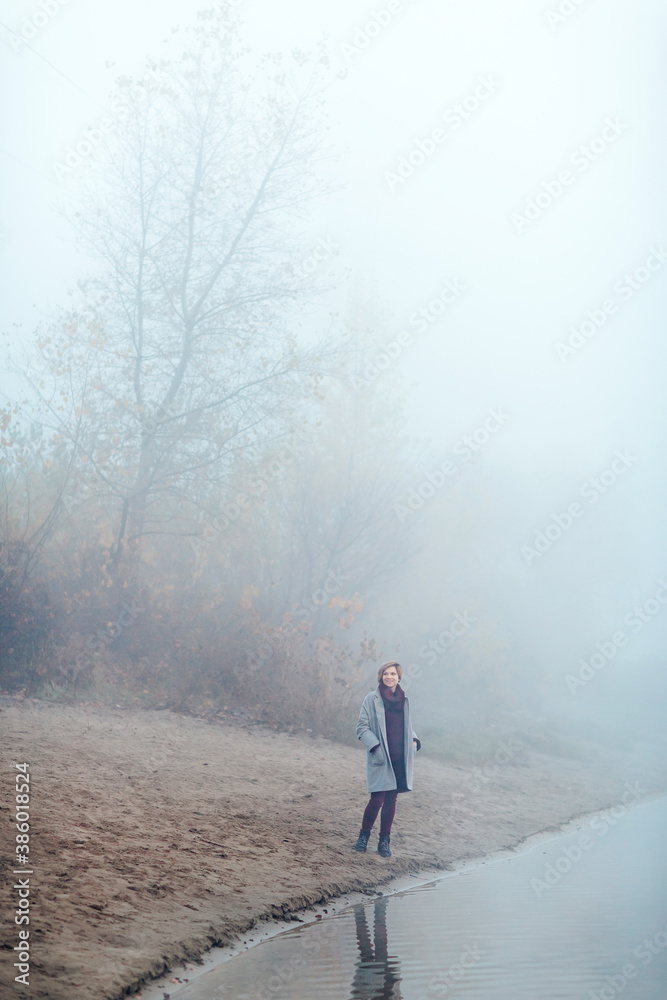 A girl runs along the shore of the lake in a foggy morning. She is having fun and has a good mood