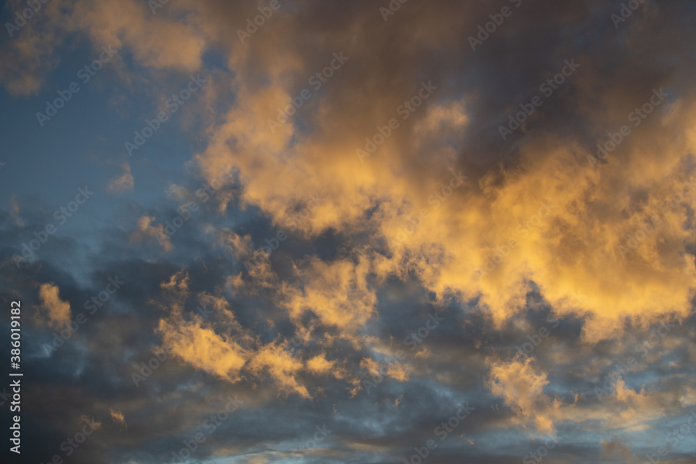 Sunset evening blue sky with fluffy light orange yellow clouds against a background of dark clouds. Different shapes