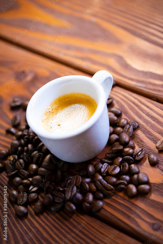 Overhead view of a freshly brewed mug of espresso coffee on rustic wooden background with woodgrain texture and roasted coffee beans Overhead view of a freshly brewed mug of espresso coffee on rustic wooden background with woodgrain texture and roasted coffee beans