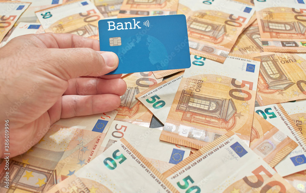 Bank card held by the hand of a white or Caucasian man on a bed of fifty euro bills