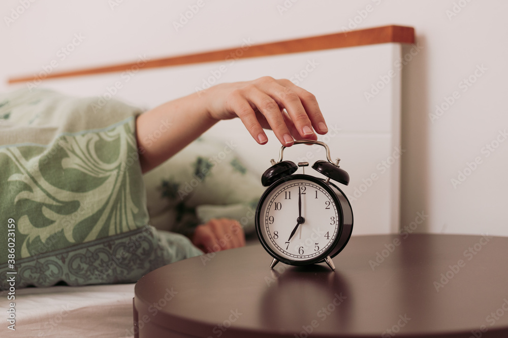 Caucasian woman in bed reaching out for analogue alarm clock to turn it
