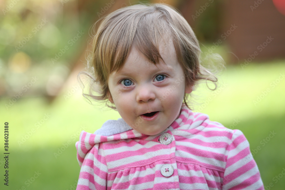 Close Up Portrait of a little 18 Month Old Girl with Big Blue Eyes and Curly Hair, a girl Playing Outside, Funny Face Expression, Happy baby Close Up Portrait of a little 18 Month Old Girl with Big Blue Eyes and Curly Hair, a girl Playing Outside, Funny Face Expression, Happy baby