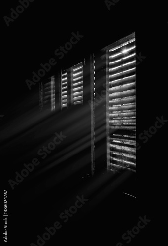 Beams of sunlight through old wooden blinds. Light coming through windows of an old abandoned house, black and white image. 