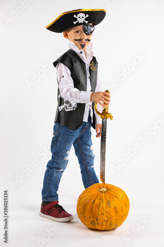 Halloween holiday. Little boy in a pirate costume and with a huge pumpkin in full lengh looking into camera on white background with empty side space photo