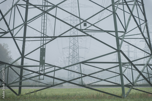 Close up view of electric power line towers align on farming field meadow. Hazy weather on flatland with low visibility