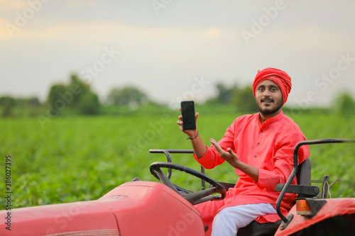 young Indian farmer showing smartphone or tablet on tractor