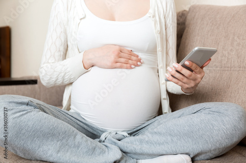 Caucasian pregnant girl using cellphone, resting on bed in home