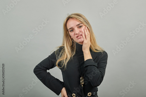 Holding hand on cheek, resting face in hands, offended displeased looks with moody expression keeps fingers countenance stands upset. Negative expressions and feelings concept. Isolated shot