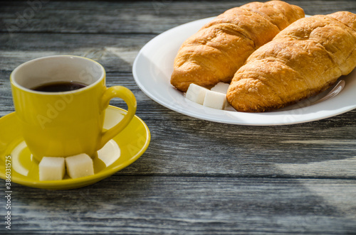 Still life with cup of coffee and croissant on the wooden background. Old retro camera and postcard are near the cup.