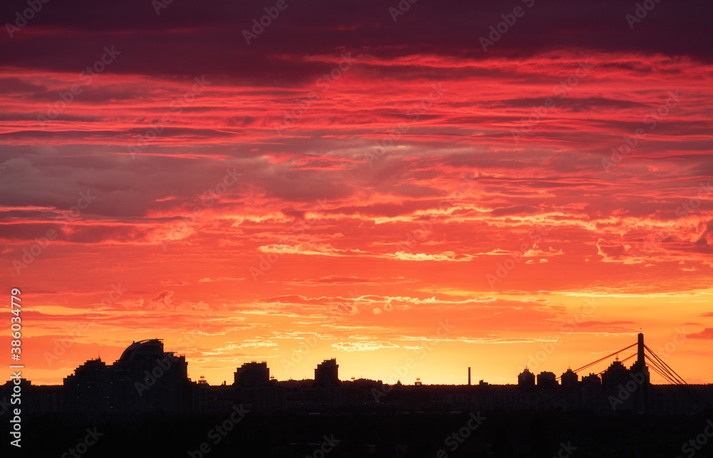 Silhouette of a Kiev city at beautiful sunset. Aerial view of buildings against colorful orange sky with sun and red clouds. Urban landscape. Background of downtown. City skyline. Cityscape