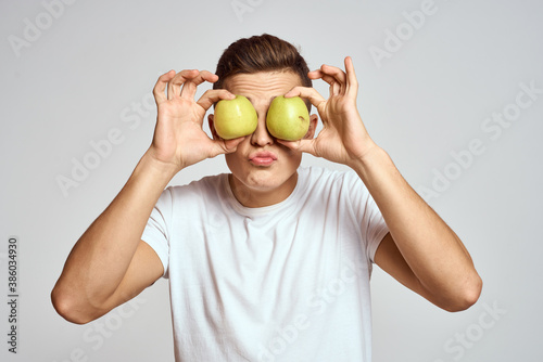 a guy with apples in his hands on a light background in a white t-shirt gesticulate with his hands smile © SHOTPRIME STUDIO