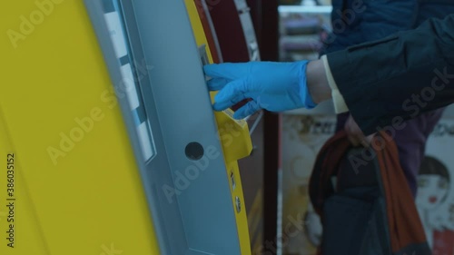 Close up female hand in protective latex glove inserting a card into an ATM machine and entering pin code. Banking service. Health medical care and safety, epidemic in the city.