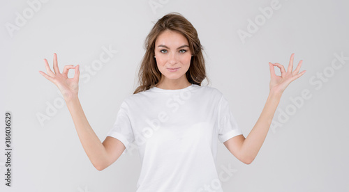 Portrait of young beautiful cute calm girl smiling looking at camera over white background with okey gesture signs