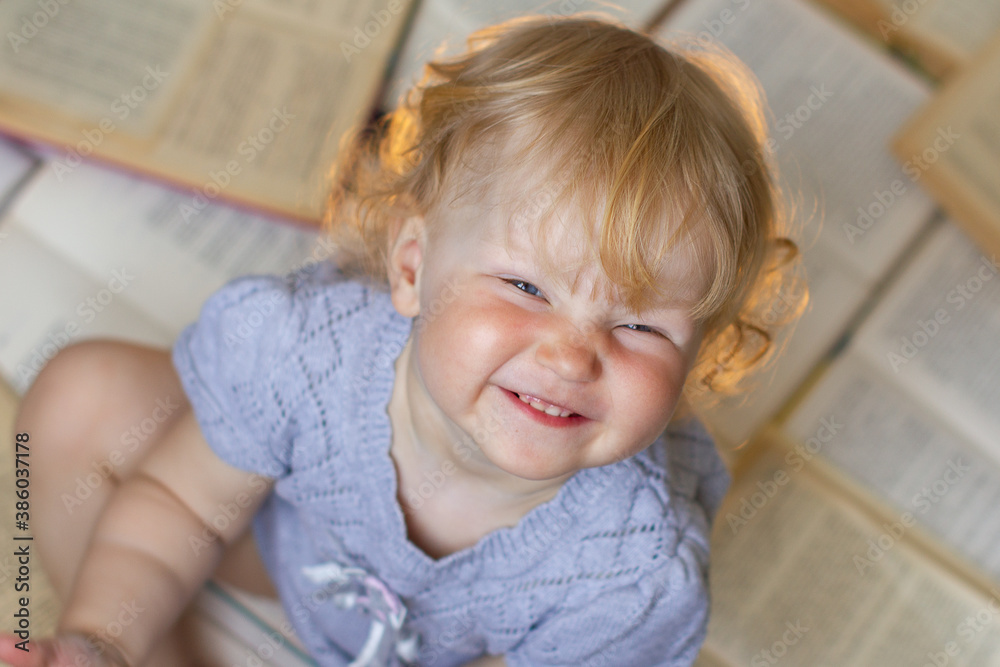 small blonde blue eyed girl boy child looking up at the camera sitting on open books soft focus small blonde blue eyed girl boy child looking up at the camera sitting on open books soft focus
