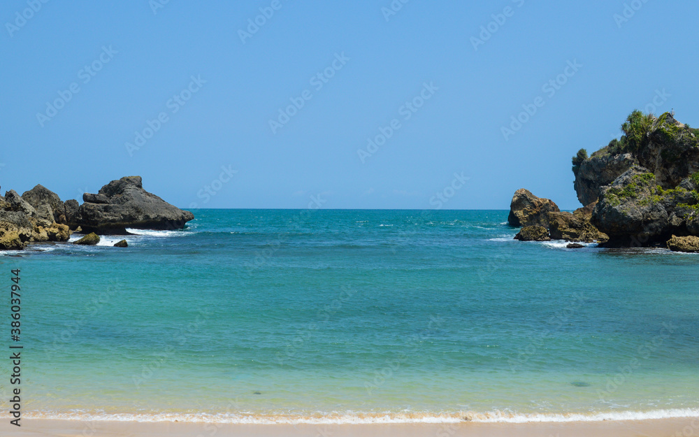 Calm blue sea with clear horizon behind rocks formation, beautiful view at Wediombo beach, Gunungkidul, Indonesia Calm blue sea with clear horizon behind rocks formation, beautiful view at Wediombo beach, Gunungkidul, Indonesia