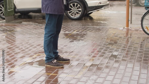 Male legs on the sidewalk under the rain. A man standing in line at the square mark. Maintaining social distance during an epidemic in the city