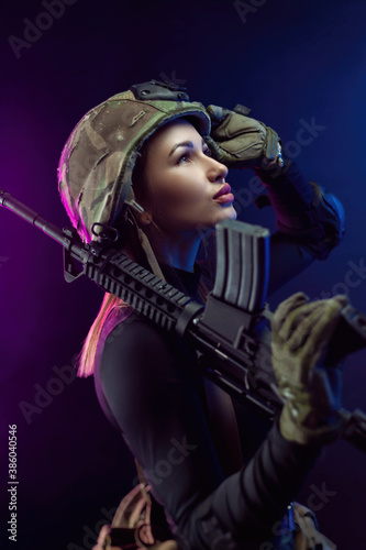 a woman in a military airsoft uniform with an American automatic rifle and a helmet on a dark background