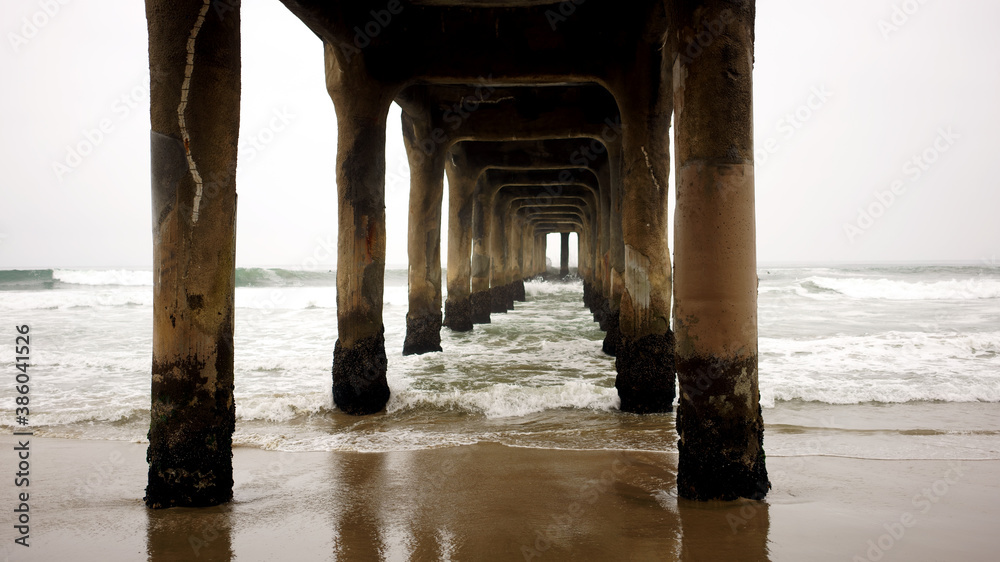 Manhattan Beach Pier with columns sand and water in frame on gloomy day.