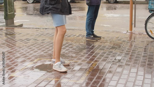 People legs on the sidewalk under the rain. A man and woman waiting in line at the square mark. Maintaining social distance during an epidemic in the city