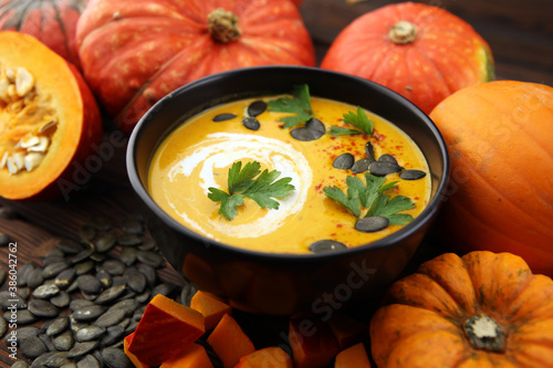 Roasted pumpkin and carrot soup with cream and pumpkin seeds on wooden background. © beats_